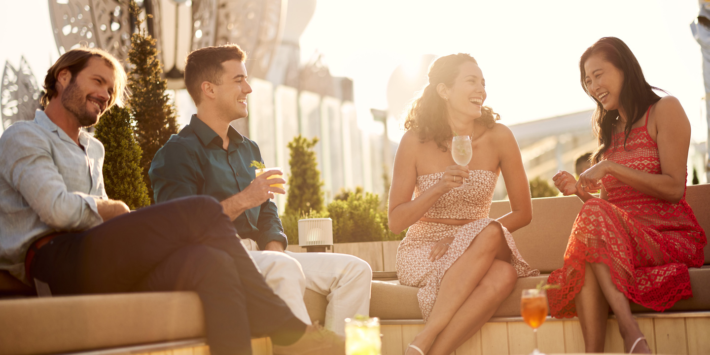 Glada gäster med drinkar på Rooftop Garden ombord på fartyget Celebrity Beyond.