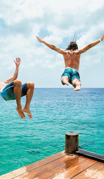 Tre killar hoppar i vattnet från en brygga i Cozumel, Mexiko.