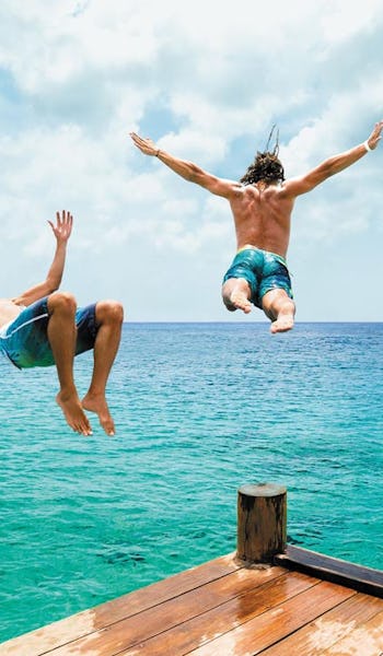 Tre killar hoppar i vattnet från en brygga i Cozumel, Mexiko.