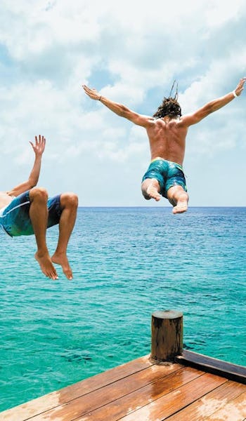 Tre killar hoppar i vattnet från en brygga i Cozumel, Mexiko.