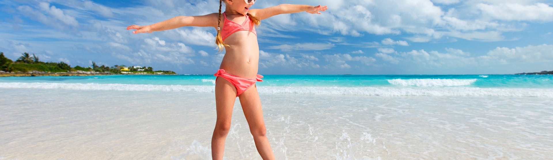 Söt liten tjej på surfbräda i strandkanten.