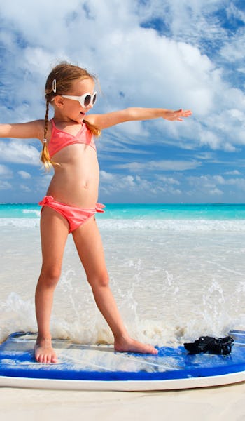 Söt liten tjej på surfbräda i strandkanten.