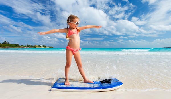 Söt liten tjej på surfbräda i strandkanten.