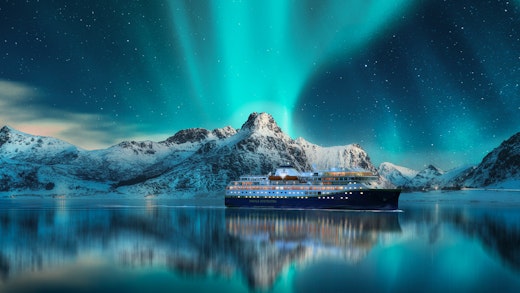 Fartyg från Havila Voyages i vattnen kring Lofoten, med norrsken som speglar sig vackert från himlen i havet.